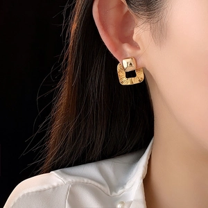 Close-up of model wearing gold-plated square earrings with irregular hammered texture