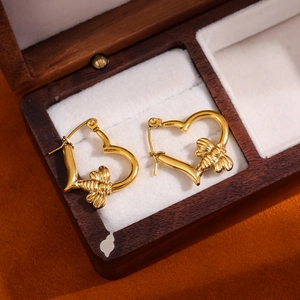 Golden heart-shaped hoop earrings with detailed bee charms on a velvet display