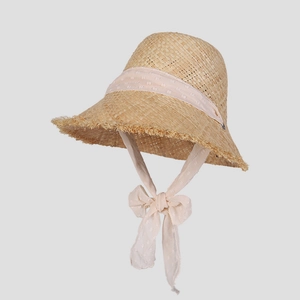 Close-up of woven raffia sun hat featuring frayed edges and pink polka dot chiffon ties