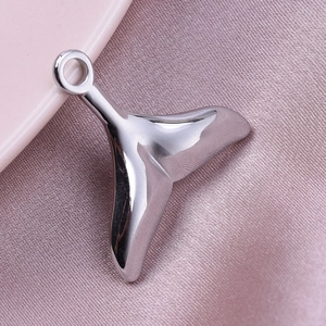 Detailed view of polished stainless steel whale tail charm on a soft pink fabric