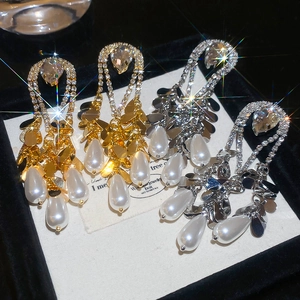 Detail of luxury teardrop pearl earrings with diamond accents and gold plating