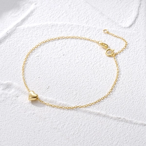Detail of a minimalist gold heart pendant bracelet with extension chain on white background