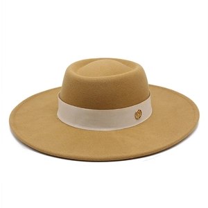 Detail of camel wool fedora hat featuring cream fabric band and gold emblem detail