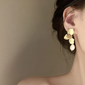Close-up of elegant gold petal and baroque pearl drop earrings worn on the ear