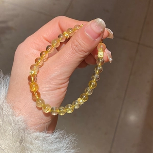 Detailed view of yellow crystal beaded bracelet with golden hollow spacer charms