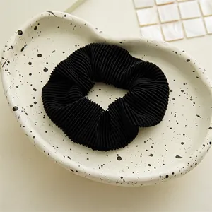 Detail of black pleated fabric scrunchie with fine texture on a white ceramic plate