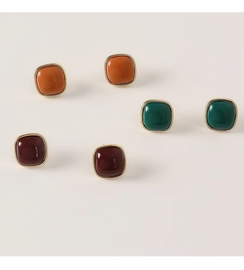 Detail of square resin stud earrings in orange, green, and red with gold metal borders