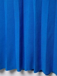Dettaglio ravvicinato del tessuto a pieghe in maglia blu di un abito a camicia