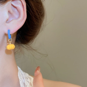 Detail of blue circular earrings with yellow pumpkin charms worn by a model