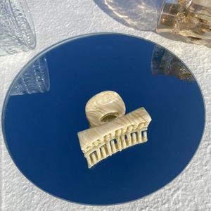 Detail of beige marble pattern hair claw clip on mirror surface with light reflection
