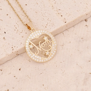 Close-up of a gold Mom pendant with micro-inlaid zircons on a textured stone surface