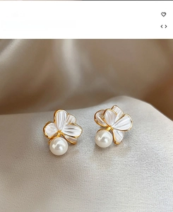 Détail de boucles d'oreilles fleurs dorées avec perles blanches sur fond de soie douce