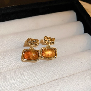 Detail of vintage resin square earrings with golden textured metal on white velvet