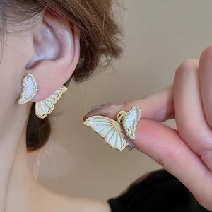 Détail macro de boucles d'oreilles papillon dorées avec émail blanc et cristaux étincelants