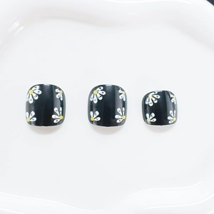 Square black press-on toenails with white daisy floral design and yellow accents