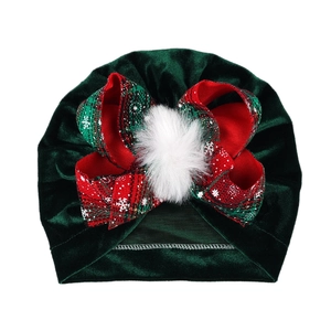 Detail view of dark green velvet baby turban with red plaid bow and white snowflake print