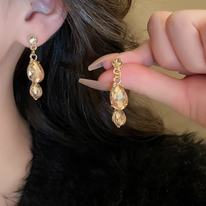Detail of luxury teardrop amber crystal earrings in golden finish on female model