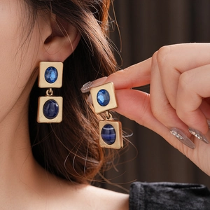 Nahaufnahme von goldenen Vintage-Ohrringen mit blauen Edelsteinen im quadratischen Design