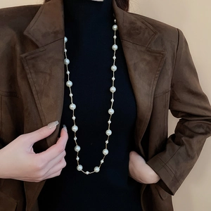 Detail of elegant faux pearl necklace with gold chain layered on a black turtleneck sweater