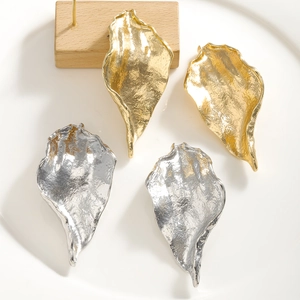 Detailed view of large gold and silver leaf earrings with irregular hammered metal texture