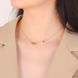 Gros plan d'un collier pendentif cœur 3D doré porté avec un blazer beige chic