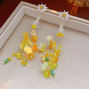 Vue détaillée des boucles d'oreilles à pompon fleur jaune et cristaux sur velours