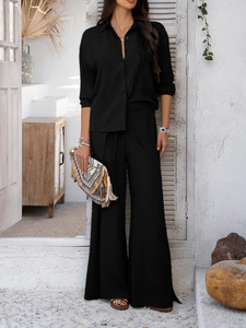 Detail of a casual black long-sleeve shirt and wide-leg trousers set with woven clutch bag