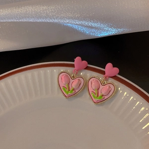 Detail of pink tulip heart earrings in gold-tone setting on decorative white plate