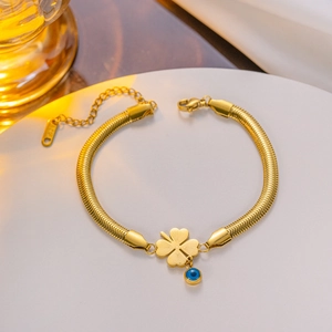 Gold snake chain bracelet with clover pendant and blue evil eye bead on white stand