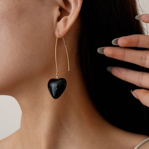 Close-up of elegant gold hook earring with black heart pendant on female model