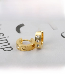 Close-up of gold huggie earrings with three inlaid zircons on a sleek steel finish