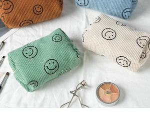 Multiple colorful corduroy cosmetic bags with smiley faces on a white fabric background