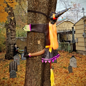 Outdoor Halloween witch decoration hugging a tree with colorful fabrics and golden leaves