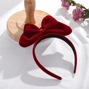 Détail d'un serre-tête en velours rouge avec grand nœud sur un support en bois et fleurs