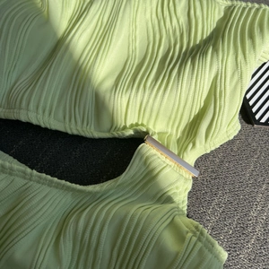 Detail of light green textured fabric with a gold metal connector on a cutout swimsuit