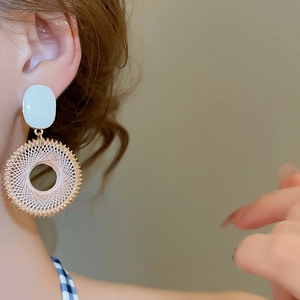 Dettaglio di orecchini pendenti tondi intrecciati su una modella con accenti bianchi e oro