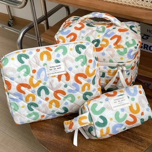 Three-piece quilted cotton cosmetic bag set with colorful abstract pattern on a wooden stool