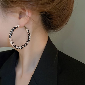 Close-up of model wearing large leopard print hoop earrings with textured finish