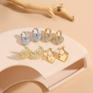 Detailed set of gold heart and moon zircon earrings arranged on a soft beige arch display