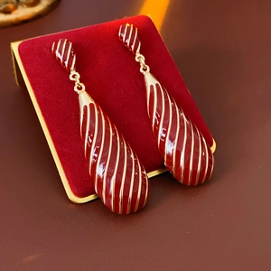 Détail de boucles d'oreilles gouttes rouges aux rayures dorées sur support velours