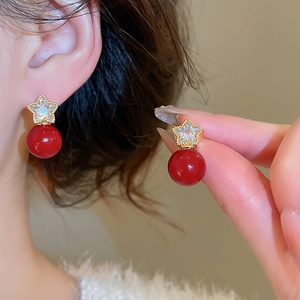 Close-up of gold-plated star zircon stud earrings with red pearl beads worn on ear