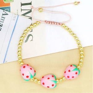 Close-up of strawberry beaded bracelet with pink adjustable cord and gold metal accents