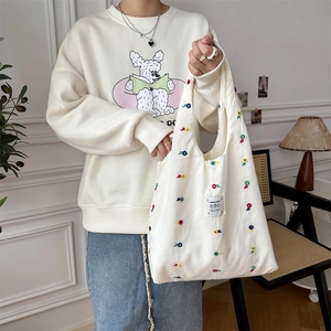 Detail of off-white canvas tote bag with floral embroidery held by model in casual style