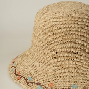 Detailed view of floral vine embroidery on the brim of a beige raffia sun hat