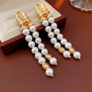 Detail view of vintage pearl drop earrings with golden engraved hooks on leather background