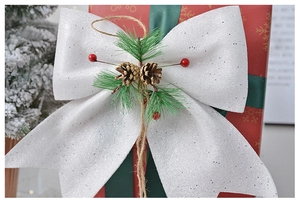 Close-up of white glitter Christmas bow with pine needles, cones and berries on a red gift box