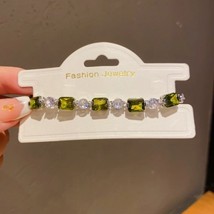 Detailed view of silver bracelet with emerald green gems and round crystals on a display card