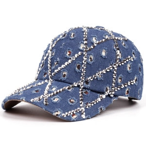 Detail of blue denim baseball cap featuring distressed holes and silver metal rivets