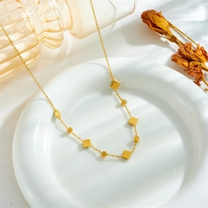 Elegant gold stainless steel necklace with emerald square charms in a white ceramic dish
