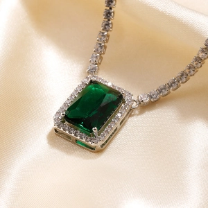 Macro shot of rectangular emerald pendant with zircon halo on champagne silk background